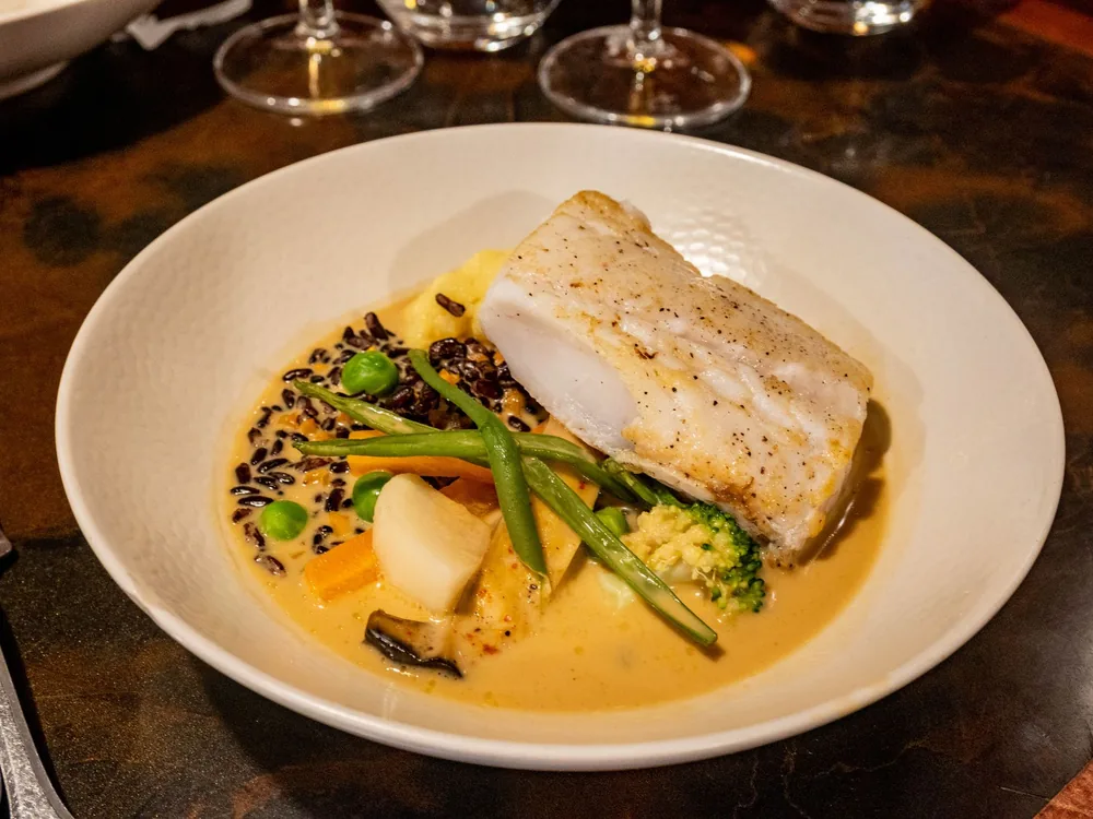 A white fish fillet with vegetables in a creamy sauce, served in a shallow bowl