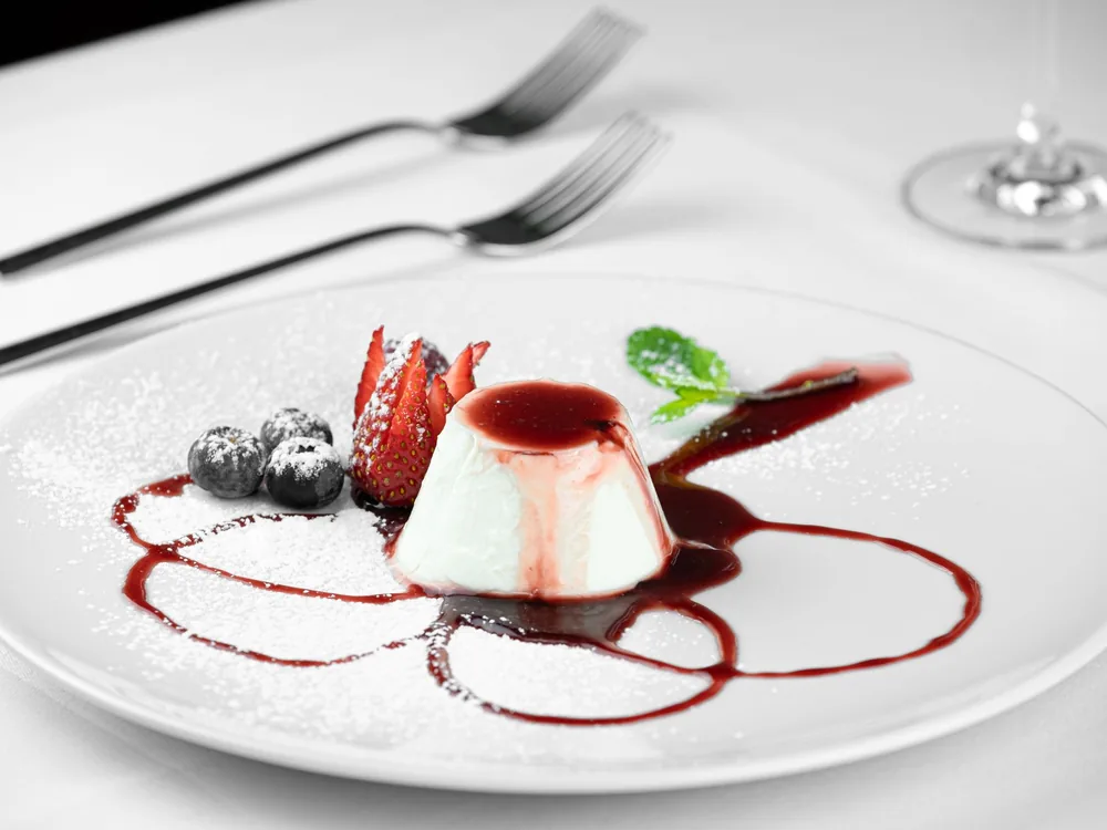 A panna cotta with fresh berries and a red berry sauce on a white plate